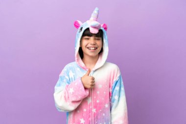 Little kid wearing a unicorn pajama isolated on purple background giving a thumbs up gesture