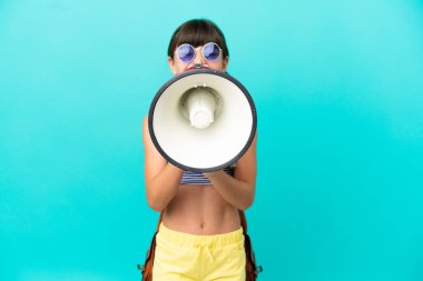 Little caucasian kid going to the beach isolated on blue background shouting through a megaphone
