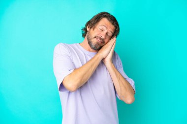 Senior dutch man isolated on blue background making sleep gesture in dorable expression
