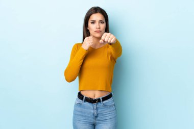 Kafkasyalı genç bir kadın, mavi arka planda yalıtılmış bir şekilde dövüşüyor.