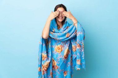 Young Moroccan woman with traditional costume isolated on blue background covering eyes by hands and smiling