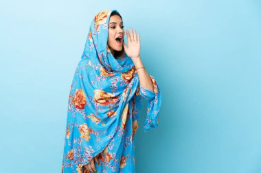 Young Moroccan woman with traditional costume isolated on blue background shouting with mouth wide open to the side