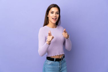 Tecrit edilmiş arka planda genç beyaz bir kadın ön tarafı işaret ediyor ve gülümsüyor.