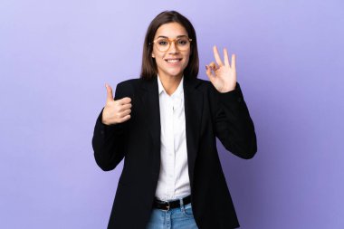 Business woman isolated on purple background showing ok sign and thumb up gesture