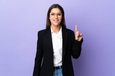 Business woman isolated on purple background showing and lifting a finger in sign of the best