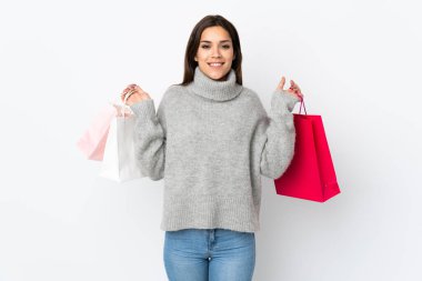 Beyaz arka planda izole edilmiş genç beyaz bir kadın alışveriş torbaları tutuyor ve gülümsüyor.