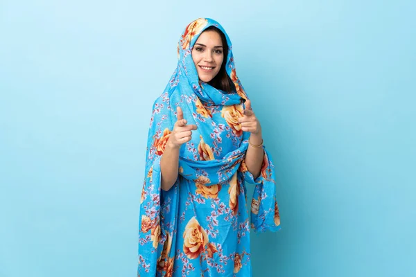 Young Moroccan woman with traditional costume isolated on blue background pointing to the front and smiling