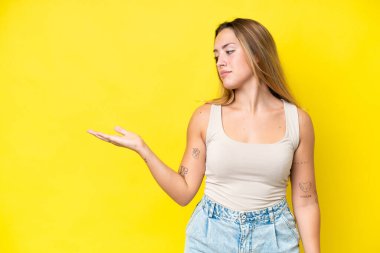 Sarı arka planda izole edilmiş genç, beyaz bir kadın. Kopyalama alanını şüphe ile tutuyor.