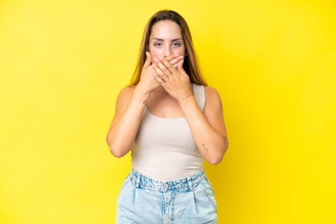 Sarı arka planda izole edilmiş genç beyaz kadın elleriyle ağzını kapatıyor.