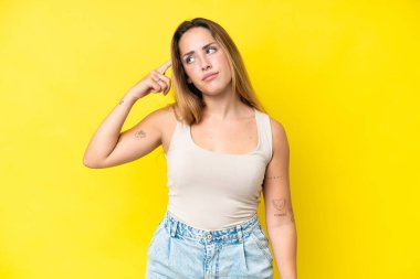 Sarı arka planda izole edilmiş genç beyaz kadın deliliğin jestini yapıyor. Parmağını kafaya koyuyor.