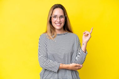 Sarı arka planda izole edilmiş genç beyaz kadın mutlu ve dik duruyor.