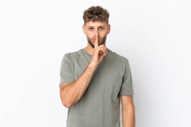 Beyaz arka planda izole edilmiş beyaz tenli yakışıklı bir adam sessiz bir jest işareti gösteriyor. Parmağını ağzına sokuyor.