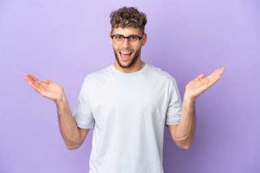 Delivery caucasian man isolated on purple background with shocked facial expression