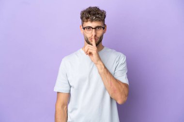 Delivery caucasian man isolated on purple background showing a sign of silence gesture putting finger in mouth