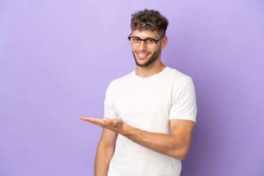 Delivery caucasian man isolated on purple background presenting an idea while looking smiling towards