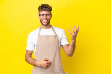 Restaurant waiter blonde man isolated on yellow background making guitar gesture