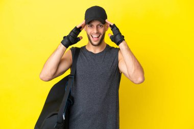 Young sport blonde man with sport bag isolated on yellow background with surprise expression
