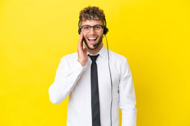 Telemarketer blonde man working with a headset isolated on yellow background with surprise and shocked facial expression