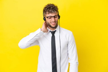 Telemarketer blonde man working with a headset isolated on yellow background with neckache
