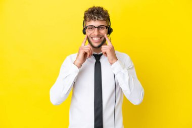 Telemarketer blonde man working with a headset isolated on yellow background smiling with a happy and pleasant expression