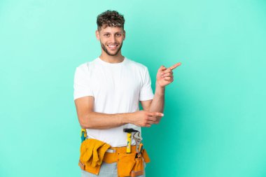 Genç elektrikçi sarışın adam yeşil arka planda izole edilmiş bir şekilde parmak ucunda bir ürün sunuyor.