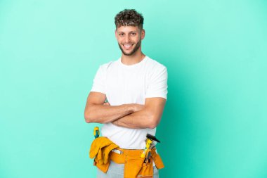 Young electrician blonde man isolated on green background with arms crossed and looking forward
