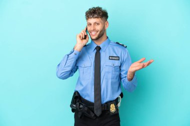 Young police blonde man isolated white on blue background keeping a conversation with the mobile phone with someone