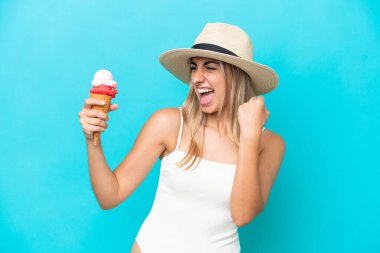 Young caucasian woman in swimsuit with a cornet ice cream isolated on blue background celebrating a victory