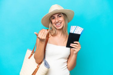 Young caucasian woman in swimsuit holding a passport isolated on blue background inviting to come with hand. Happy that you came