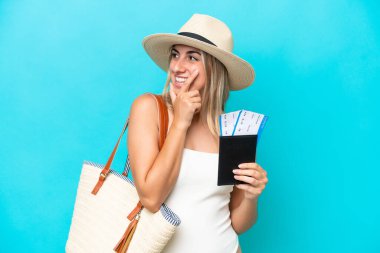Young caucasian woman in swimsuit holding a passport isolated on blue background thinking an idea and looking side