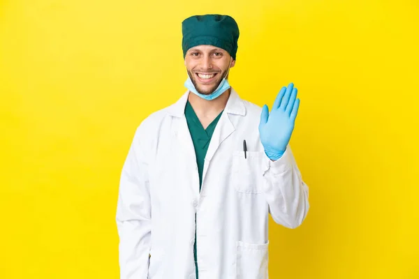 Χειρούργος Ξανθός Άντρας Πράσινη Στολή Απομονωμένος Κίτρινο Φόντο Χαιρετώντας Χέρι — Φωτογραφία Αρχείου