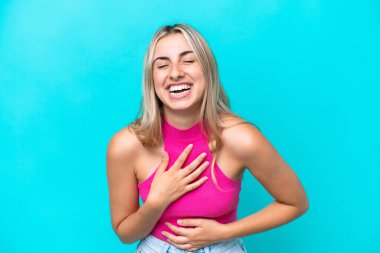 Mavi arka planda izole edilmiş genç beyaz kadın çok gülümsüyor.