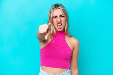 Mavi arka planda izole edilmiş genç beyaz kadın hayal kırıklığına uğramış ve ön tarafı işaret ediyor.