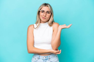 Kafkasyalı genç bir kadın mavi arka planda izole edilmiş. Şüpheleri var.