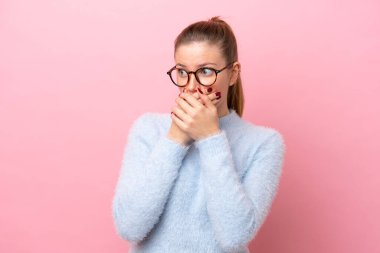 Pembe arka planda izole edilmiş genç beyaz kadın ağzını kapatıyor ve yan tarafa bakıyor.