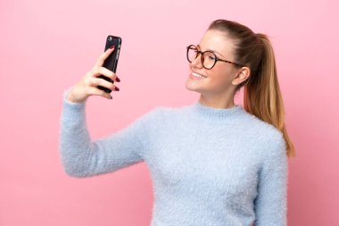 Pembe arka planda izole edilmiş beyaz bir kadın selfie çekiyor.