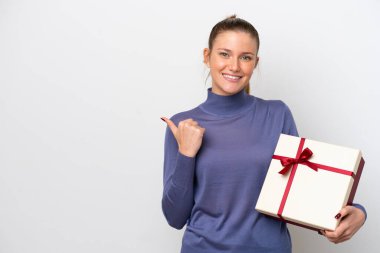 Beyaz arka planda izole edilmiş bir hediye taşıyan beyaz bir kadın bir ürünü sunmak için kenarı işaret ediyor.