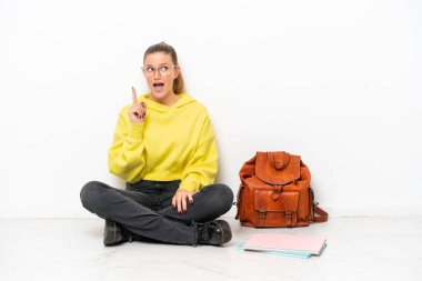 Young student caucasian woman sitting one the floor isolated on white background thinking an idea pointing the finger up