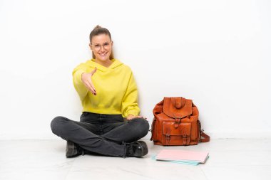 Young student caucasian woman sitting one the floor isolated on white background shaking hands for closing a good deal