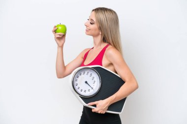 Pretty blonde woman isolated on white background with weighing machine and with an apple