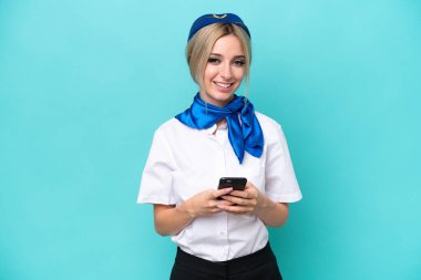 Airplane blonde stewardess woman isolated on blue background sending a message with the mobile