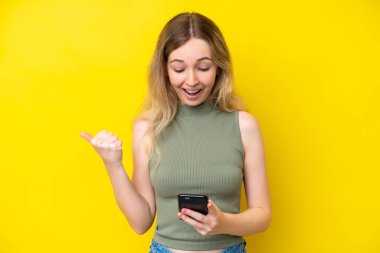 Blonde English young girl isolated on yellow background surprised and sending a message
