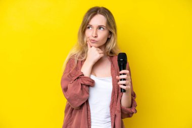 Young singer caucasian woman picking up a microphone isolated on yellow background having doubts