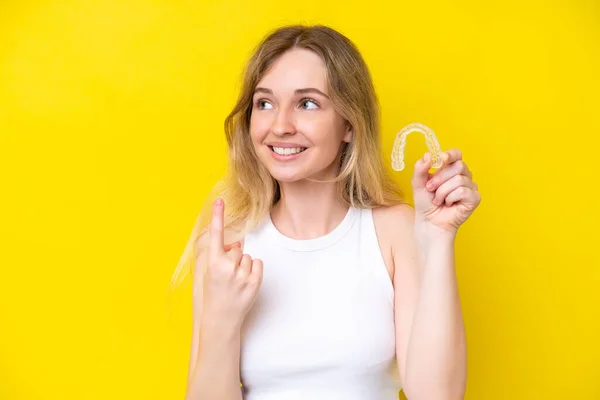Blonde English Young Girl Holding Invisible Braces Isolated Yellow Background — Stock fotografie