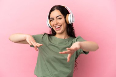 Genç beyaz kadın pembe arka planda izole edilmiş müzik ve dans dinliyor.