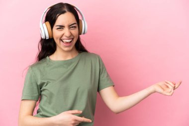 Genç beyaz kadın pembe arka planda izole edilmiş müzik dinliyor ve gitar hareketi yapıyor.