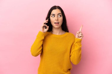 Young caucasian woman using mobile phone isolated on pink background thinking an idea pointing the finger up