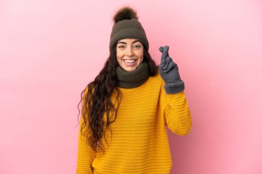 Young caucasian girl with winter hat isolated on purple background with fingers crossing and wishing the best