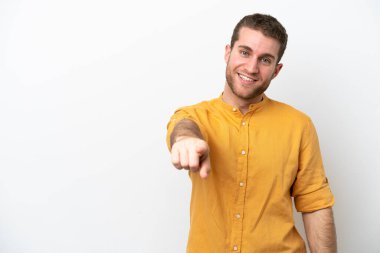 Beyaz arka planda izole edilmiş genç beyaz adam mutlu bir ifadeyle ön tarafı işaret ediyor.