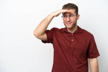 Beyaz arka planda izole edilmiş genç beyaz bir adam bir şeye bakmak için çok uzaklara bakıyor.